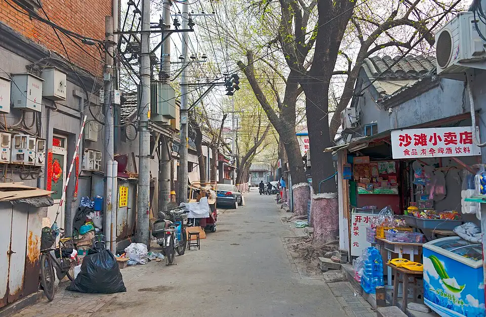 Hutong-Gasse in Peking mit Fahrradfahrern und Geschäften